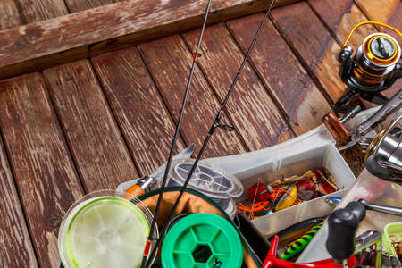 Different fishing tacles with rod and reels on wooden brown background. Mockap for advertisment and publishing.の写真素材