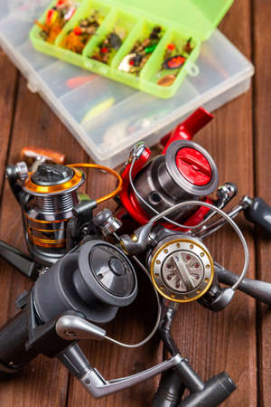 Different fishing tacles with lures and reels on wooden brown background with place for text. Design...