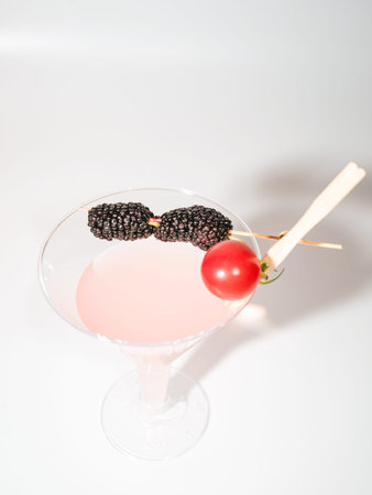 A pink alcoholic beverage in a cocktail glass topped with a bamboo skewer holding fresh blackberries...