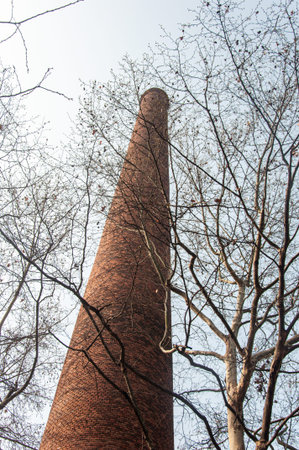 Vertical low angle shot looking up at a tall, round red brick factory chimney rising through the...