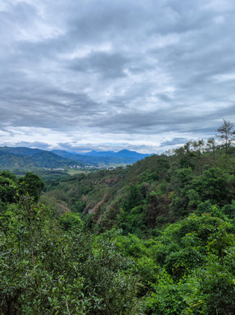 A vast mountainous landscape perspective showing green valleys and distant hills under a moody...
