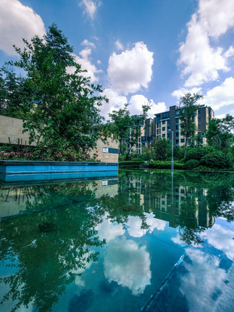 A vertical landscape view of a quiet pool of water reflecting the sky and buildings in an upscale...