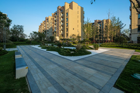 A landscape view of a modern stone-paved walkway with geometric patterns, surrounded by manicured...