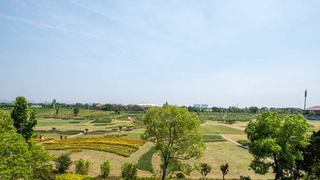 A wide-angle landscape shot of a meticulously maintained park with geometric flower beds, manicured...