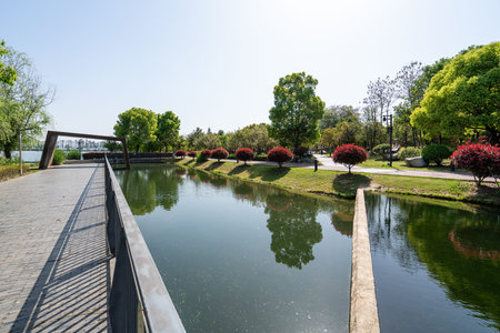 A modern wooden walkway over a calm lake in a city park. The image conveys outdoor design, leisure,...