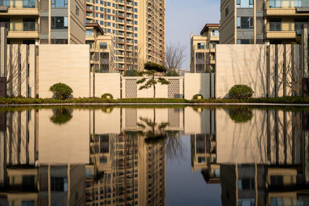 Description: A serene water feature in a community park, reflecting modern buildings and trees. The...