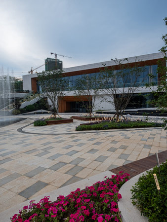A view of a modern plaza with intricate stone paving under an overcast sky. The image conveys...