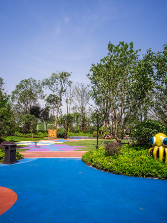 Description: A vibrant, colorful playground path winding through a lush city park on a sunny day. The image conveys recreation, design, and nature. High-quality photography.の写真素材