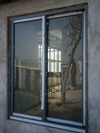 Wuhan, China - March 24, 2025: Glass window reflecting pedestrians walking outside an unfinished...