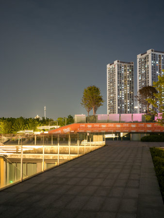 Wuhan, China - June 11, 2025: Elevated paved walkway featuring glass railings and warm yellow...