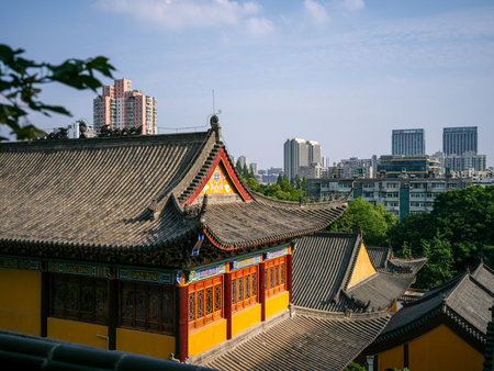 Wuhan, China - May 19, 2025: Traditional Chinese temple building featuring yellow roof tiles and ornate wooden eaves. The image contrasts historic cultural architecture in the foreground with modern residential high-rise buildings in the background.のeditorial素材