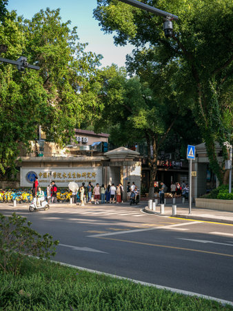 Wuhan, China - June 16, 2025: Main entrance gate of the Institute of Hydrobiology Chinese Academy of Sciences bordered by large green trees. The image captures pedestrians walking, electric scooters and traffic signs on a paved urban street.のeditorial素材