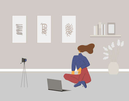 Young woman sitting on the floor with camera and laptop. Female blogger dressed in casual clothes...