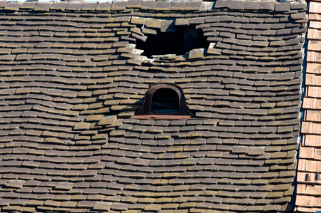 Old damaged tiled roof with broken tiles and a hole on the roofの写真素材