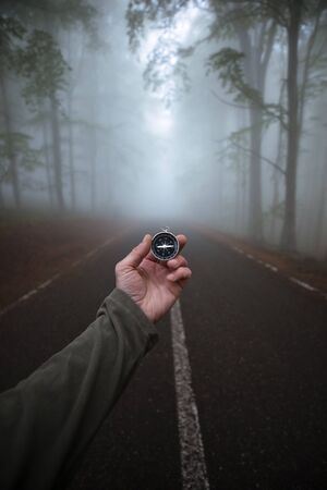 Male hand with compass on background of forest in fog, point of view.