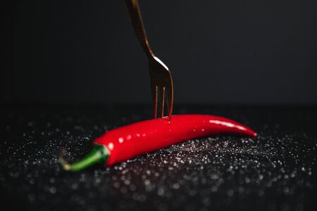A red hot chili pepper on a lucury gold fork against a dark background.の写真素材