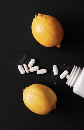 Vitamin C capsules. Pills with pill bottle and bio lemon fruit isolated on dark background. Top viewの写真素材