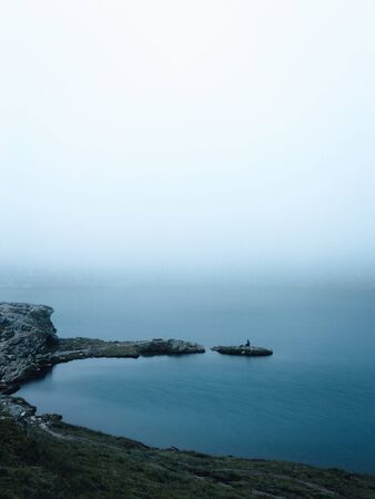 Traveler man standing on isle rock,minimalistic foggy view.の写真素材