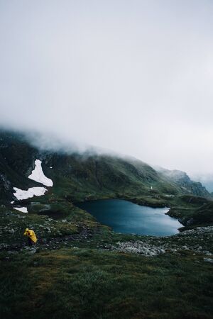 Hiker in a yellow jacket walking in a foggy mountains near the glacier Capra lakeの写真素材