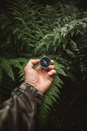 Backpacker male hand with magnetic compass on background of green forest leaves, point of viewの写真素材