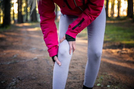 Injury from workout concept - Caucasian woman use hands hold on her painful knee while running in forest training.の写真素材
