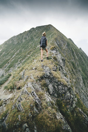 Young woman hiker standing on top of a mountain and looking away