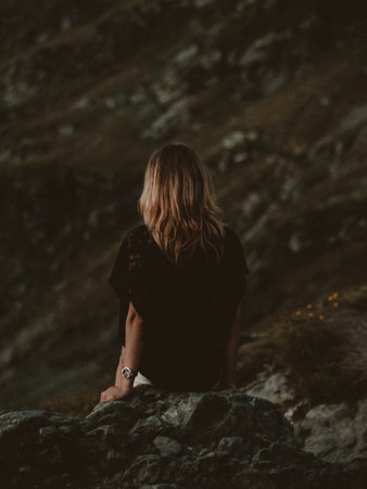 Young woman sitting on a rock in the mountains and looking at the sunsetの写真素材