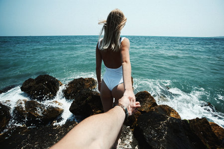 Man and woman holding hands on the background of the sea and the rocksの写真素材