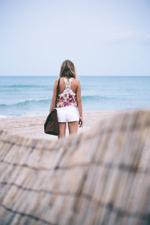Young woman in white shorts standing on the beach and looking at the seaの写真素材