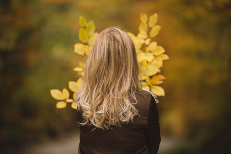 Blonde girl in autumn park with yellow leaves on her back.の写真素材