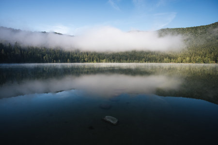 Landscape of a mountain lake with fog and clouds in the background