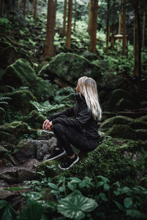 Young woman sitting on a rock in the forest, wearing a black jacket
