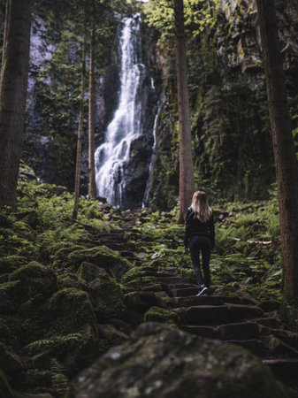 Young woman standing in front of a waterfall in the middle of the forest