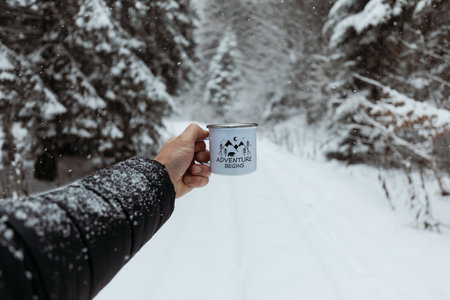 Hiker man hand holding a mug of hot drink in the winter forest.の写真素材