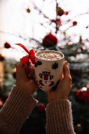 Female hands holding a cup of hot chocolate with marshmallow on Christmas tree backgroundの写真素材