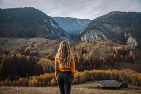 A girl in a yellow jacket stands on the top of the mountain and looks into the distance.の写真素材