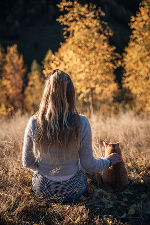 Beautiful young woman sitting on the grass in the autumn forest with her catの写真素材