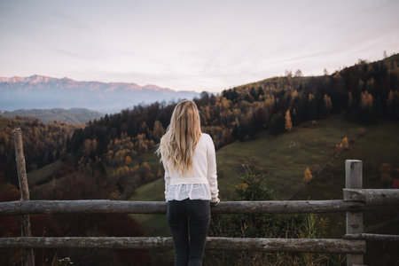 A young woman is standing on a wooden fence in the mountains.の写真素材