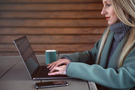 Smiling female entrepreneur sitting at a table in home terrace of a coffe shop and writing down notes and working on a laptopの写真素材