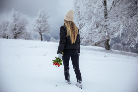 Beautiful young woman with a bouquet of red roses walking in the snowy forest. Outdoors, Valentine's day concept.の写真素材