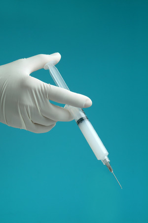 syringe with medicine being held by hand with surgical glove on blue background.の写真素材