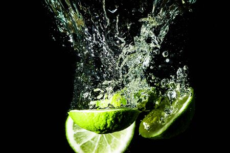 Lime slice splashing into water on black background.の写真素材