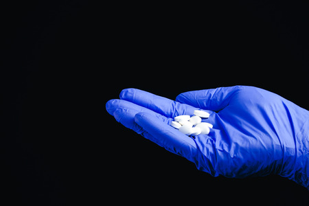 Blue latex glove hand holding pills.の写真素材