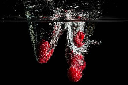 Raspberries splashing into water on black background.の写真素材