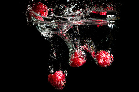 Raspberries splashing into water on black background.の写真素材