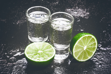 Vodka shot glass on black wet surface with limes.の写真素材
