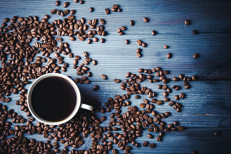 White coffee cup on blue wooden table with coffee seeds everywhere around.