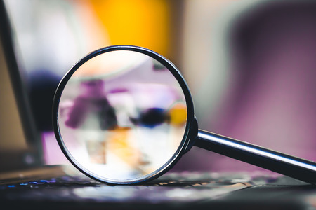 Search technology background. Magnifying glass on computer keyboard with shallow depth of field and blurred colors inside.の写真素材