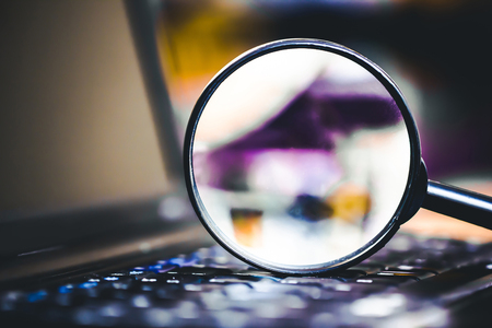 Search technology background. Magnifying glass on computer keyboard with shallow depth of field and blurred colors inside.の写真素材