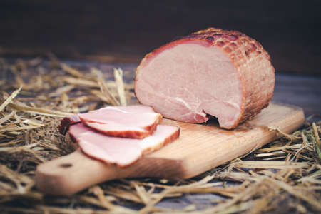 Ham on wooden desk. Rustic background with hay and meat slices.の写真素材